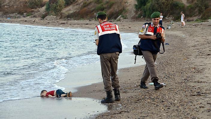 epa04909154 Turkish gendarmerie stand near by the washed up body of a refugee child who drowned during a failed attempt to sail to the Greek island of Kos, at the shore in the coastal town of Bodrum, Mugla city, Turkey, 02 September 2015. At least 11 Syrian migrants died in boat sank after leaving Turkey for the Greek island of Kos. EPA/DOGAN NEWS AGENCY ATTENTION EDITORS: PICTURE CONTAINS GRAPHIC CONTENT ; TURKEY OUT